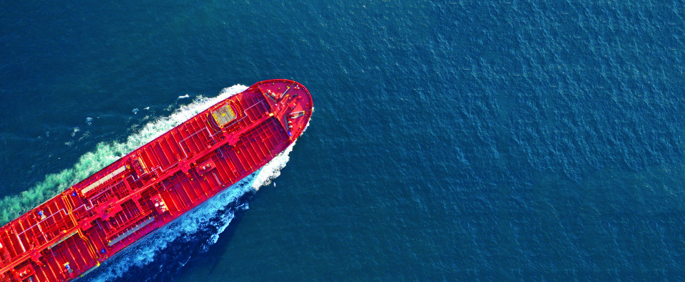 Aerial view of a red cargo ship sailing through deep blue water.